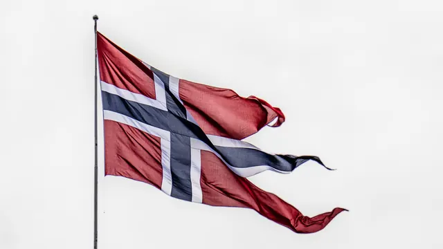 Norsk statsflagg med splitt og tunge på flaggstang i vinden